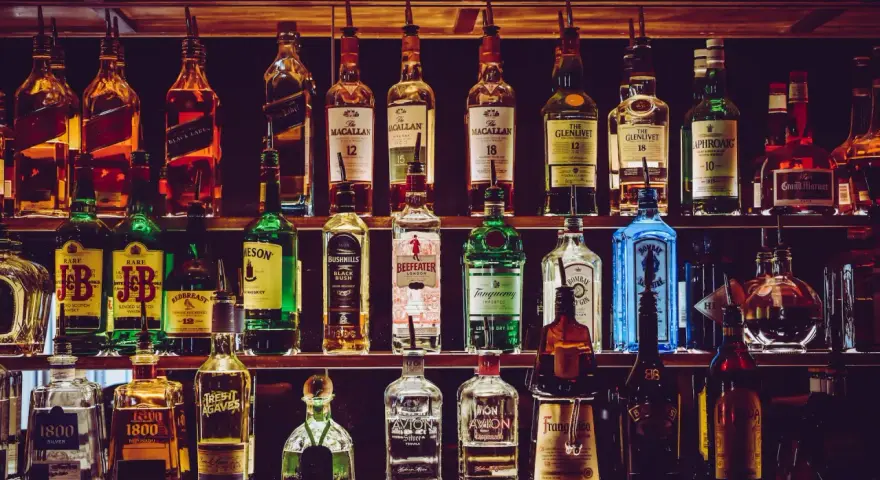 Różnorodne podstawowe alkohole do drinków: whisky, gin, tequila, likiery, stoją na półkach baru, gotowe do przygotowania koktajli.