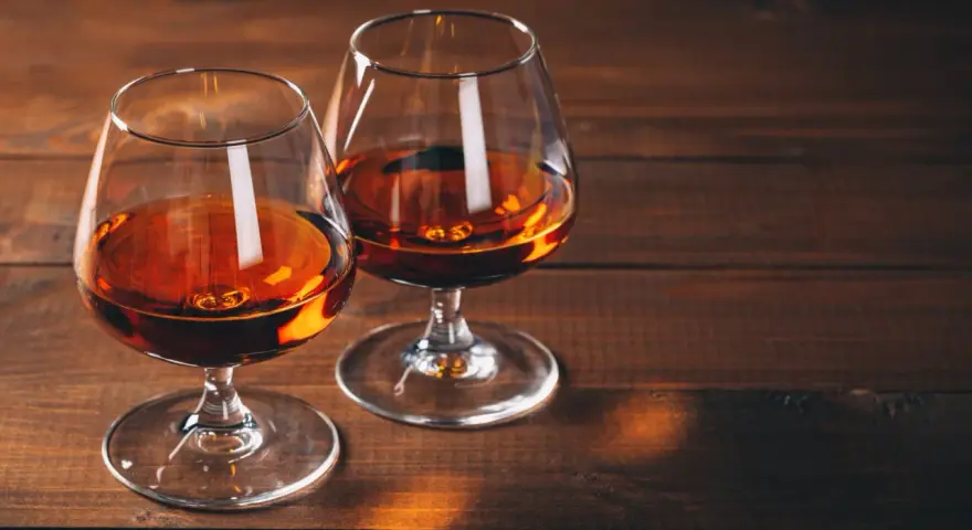 Dwa kieliszki z bursztynowym płynem, być może amerykańska whisky z kukurydzy, stoją na drewnianym stole.