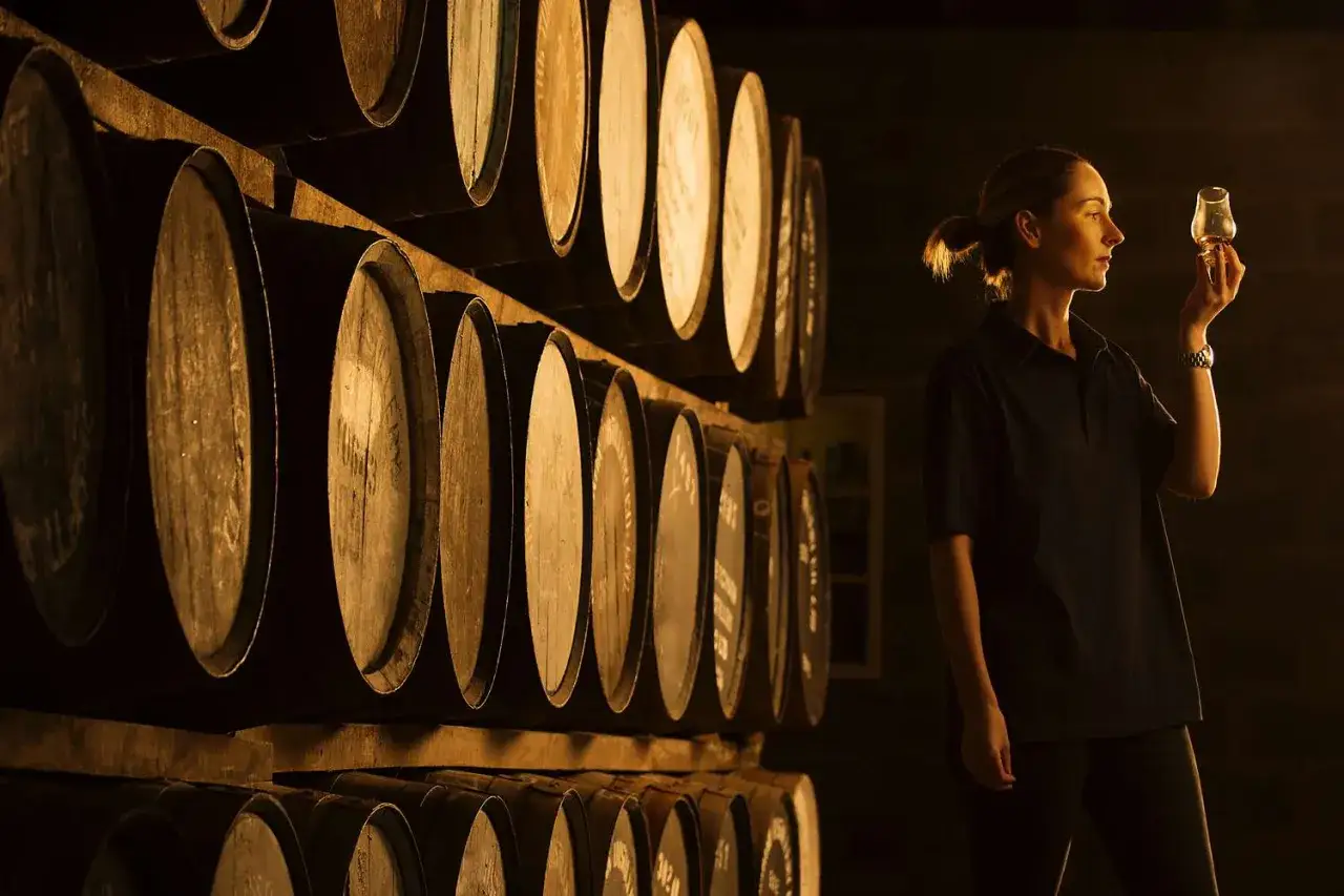 Kobieta ocenia jakość brandy i whisky w piwnicy pełnej beczek.