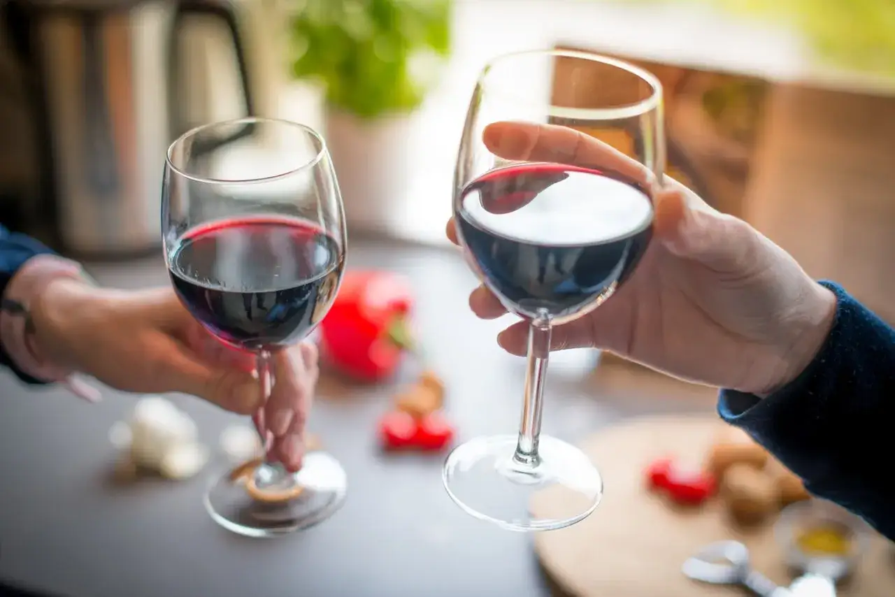 Dwie osoby wznoszą kieliszki z czerwonym winem. To klasyczne cabernet sauvignon, jakie to wino? Pełne, aromatyczne, idealne na wiecz&oacute;r.