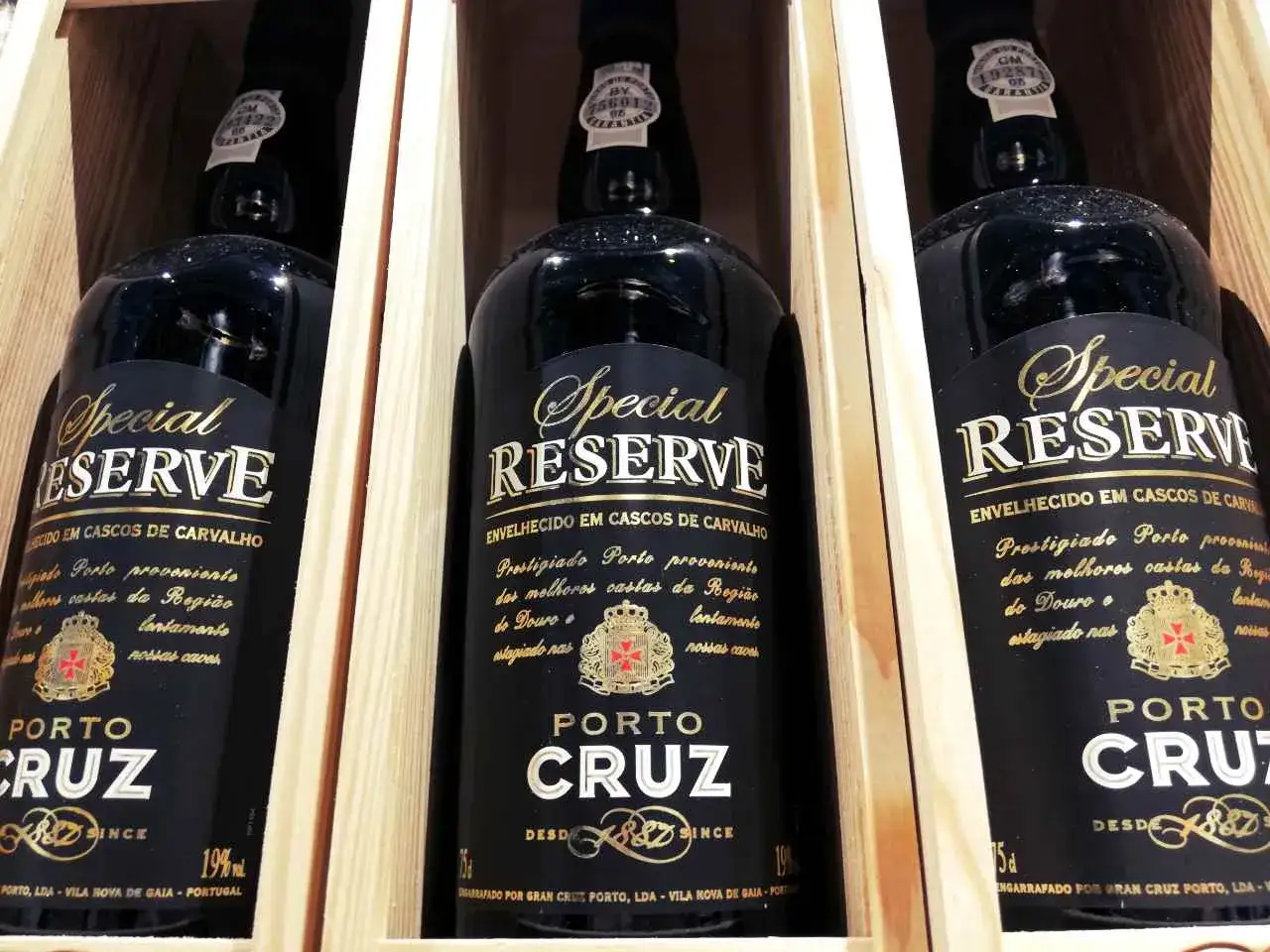 Trzy butelki p&oacute;łwytrawnego wina portugalskiego Porto Cruz Special Reserve w drewnianych skrzynkach.