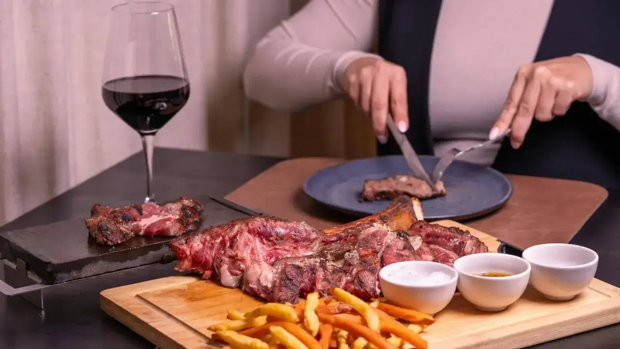 Idealne wino do dziczyzny? Czerwone, pełne, jak to z kieliszka obok soczystego steka i frytek. Ktoś kroi porcję na talerzu.