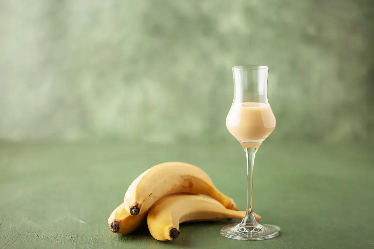 Kremowy likier bananowy w kieliszku, obok dojrzałe banany. Idealny składnik do domowego likieru bananowego przepis.