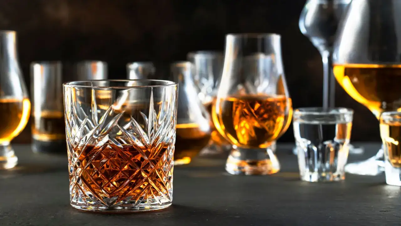 Szklanki z bursztynowym trunkiem, jak koniak i whisky, stoją na ciemnym tle.
