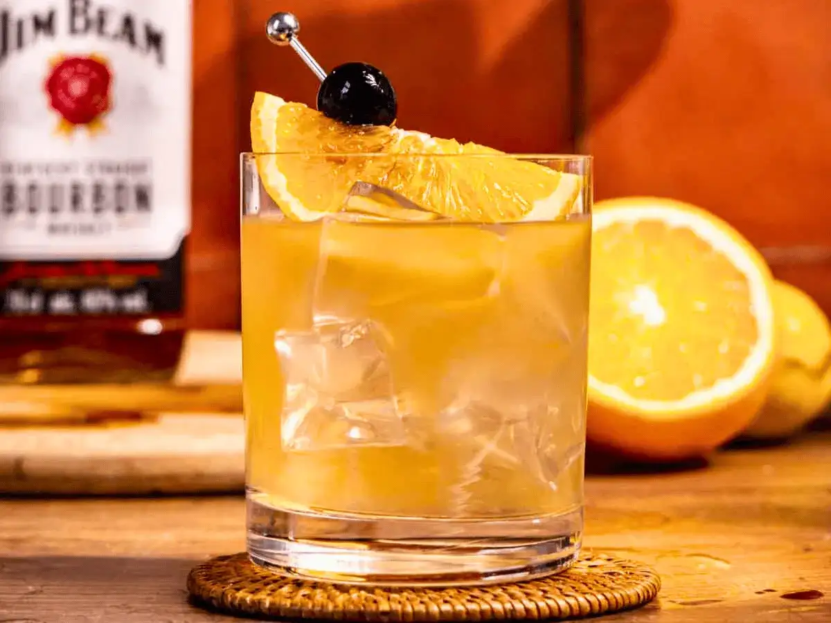 Orzeźwiający drink: whisky z cytryną, lodem i wiśnią, ozdobiony plasterkiem pomarańczy.