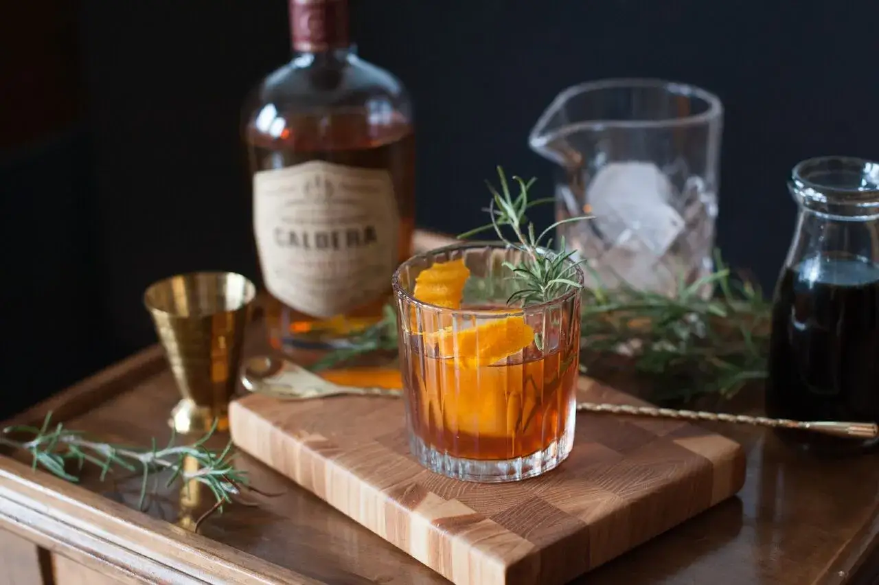 Elegancki drink z whisky i syropem klonowym, ozdobiony sk&oacute;rką pomarańczy i rozmarynem, gotowy do degustacji.