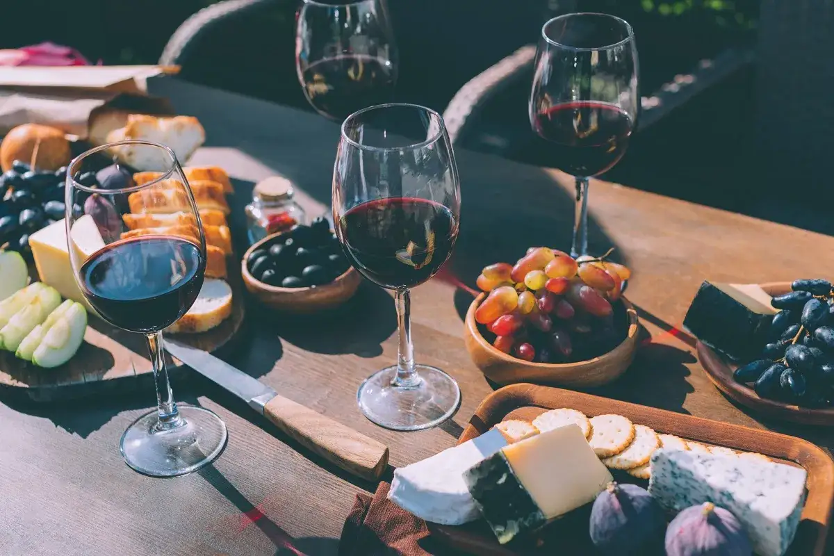 Degustacja merlot: jakie to wino? Kieliszki czerwonego wina, sery, winogrona, oliwki i pieczywo na drewnianym stole.