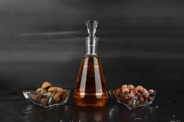Amaretto co to? Bursztynowy likier w karafce, obok miseczki z migdałami i orzechami laskowymi.