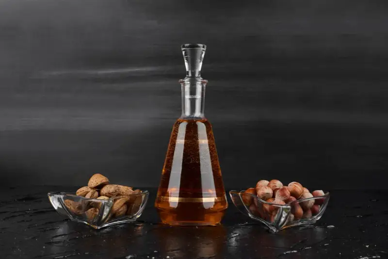 Amaretto co to? Bursztynowy likier w karafce, obok miseczki z migdałami i orzechami laskowymi.