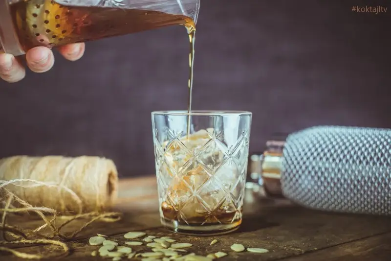 Nalewanie drinka z amaretto i wódką do szklanki z lodem. Na stole płatki migdałów i sznurek.